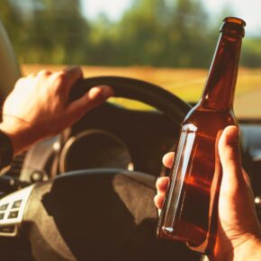 Man driving a car a holding a bottle of beer