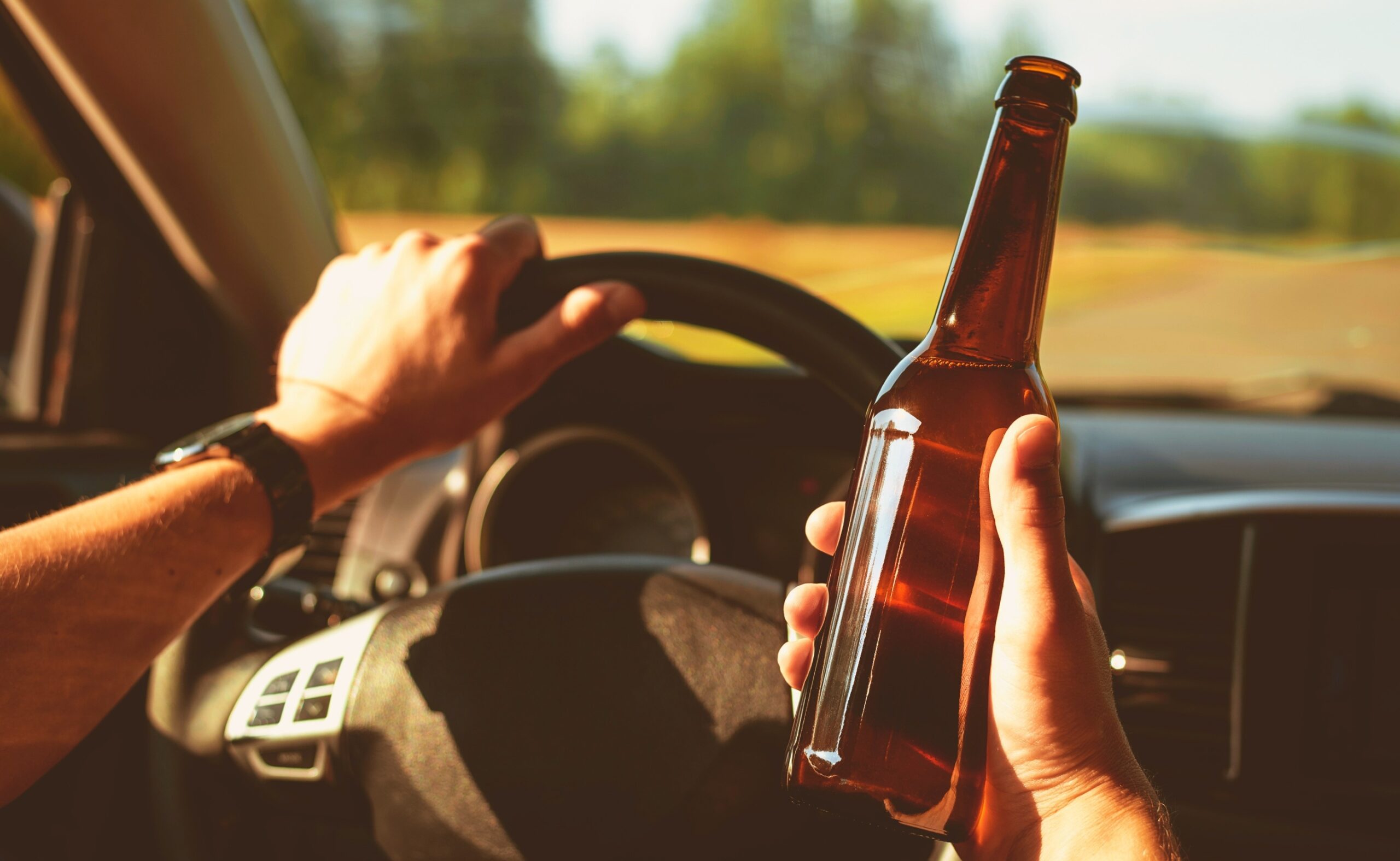 Man driving a car holding a a bottle of beer