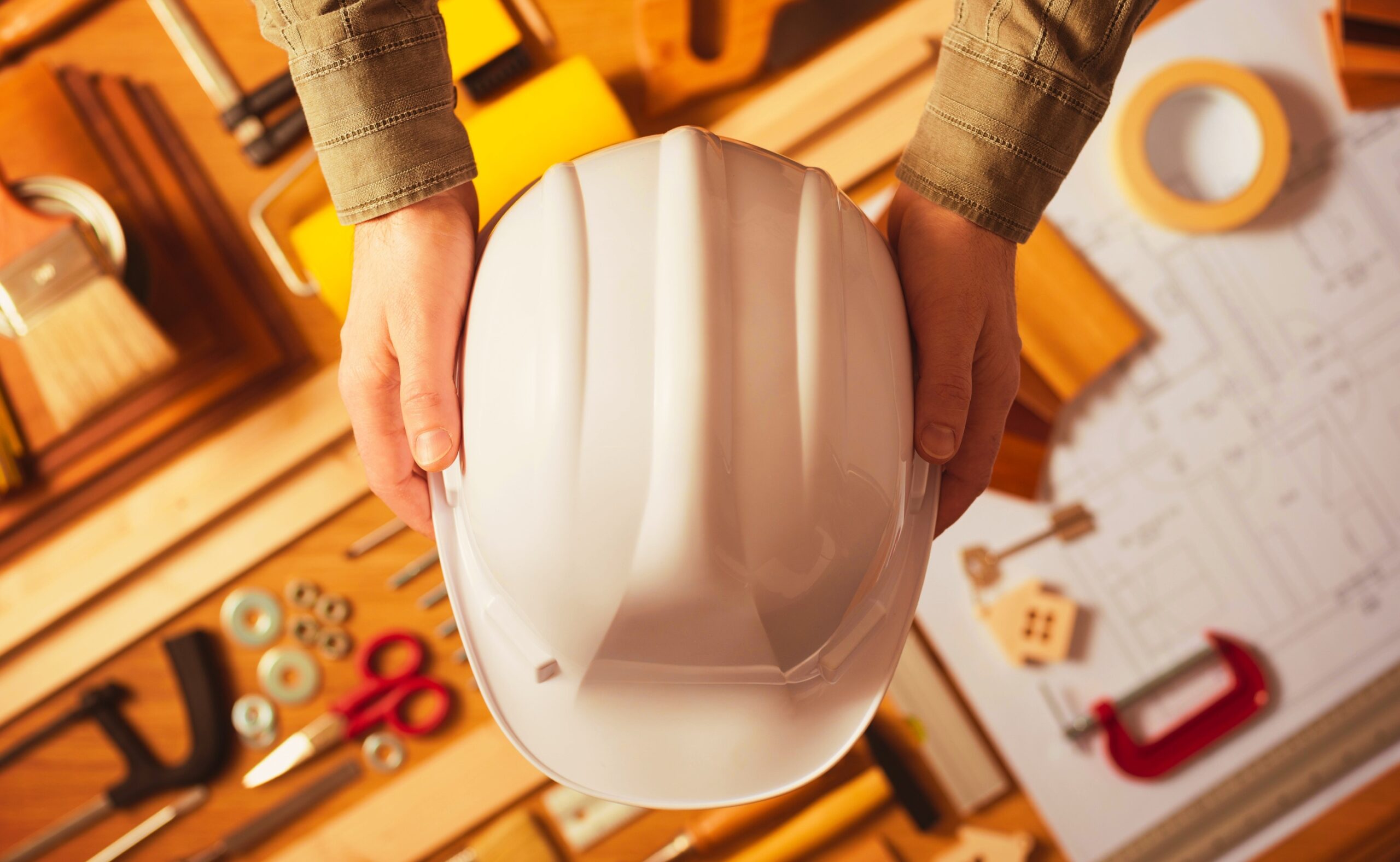 Hands holding protective safety helmet against a work table with hardware and construction tools