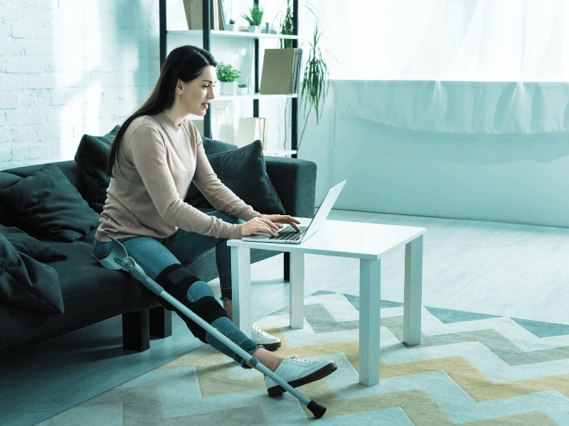 beautiful woman with broken leg having online consultation with doctor on laptop at home