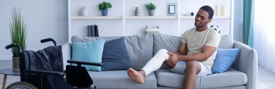 An injured dark skinned man on a sofa with bandage on his right leg