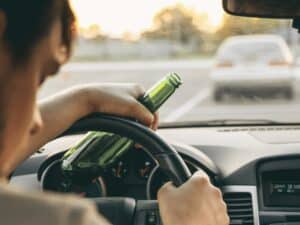 Drunk young man driving a car with a bottle of beer