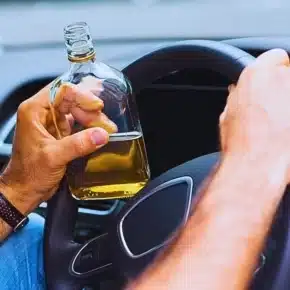 Man holding a bottle of alcohol while driving. Blackout Wednesday