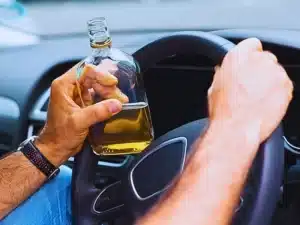 Man holding a bottle of alcohol while driving. Blackout Wednesday