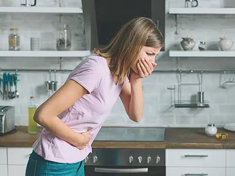 Woman in the kitchen holding her stomach and mouth feeling sick due to food poisoning. food poisoning
