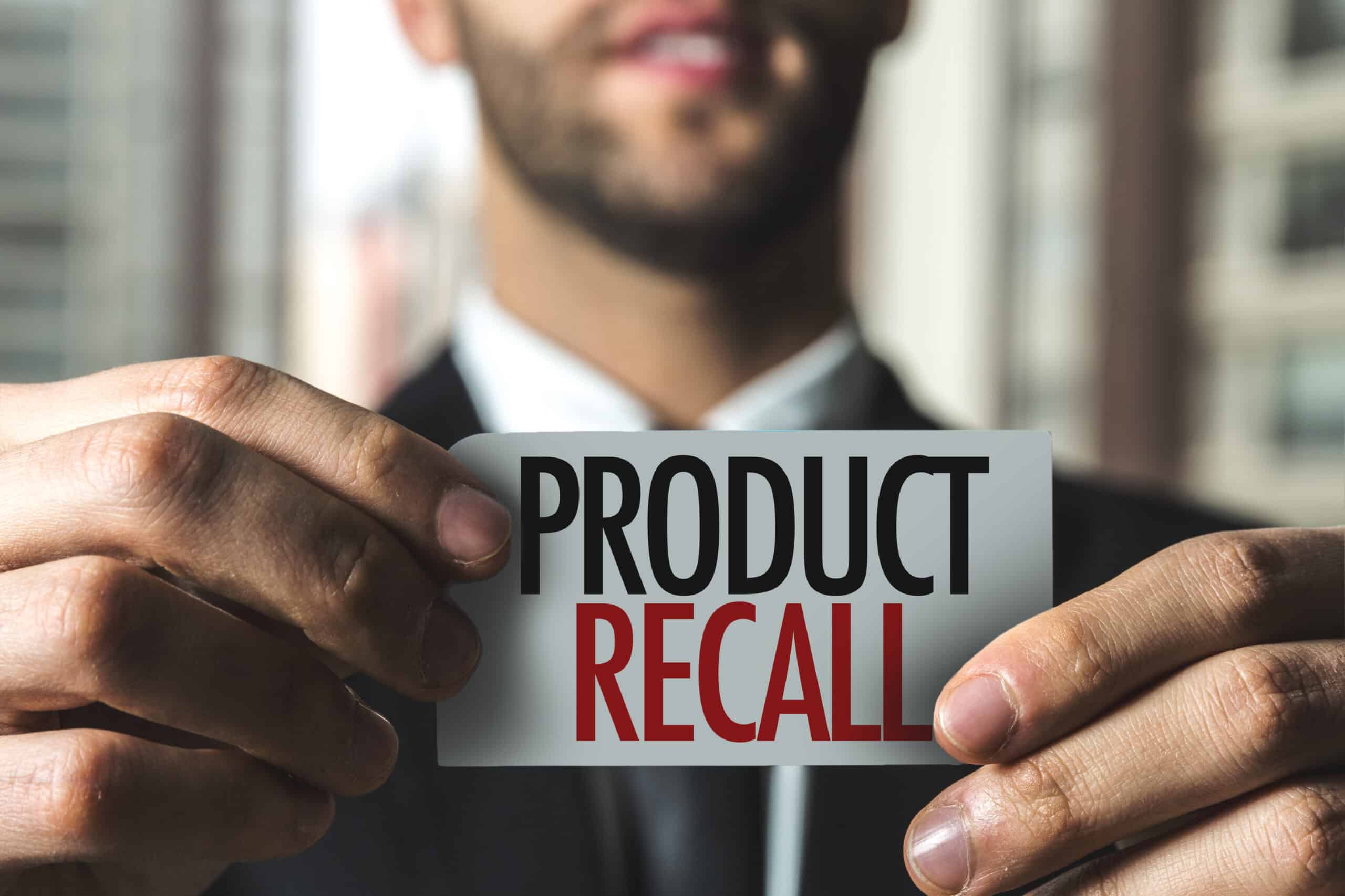 Man in suit holding a piece of paper with Product Recall printed in black and red.