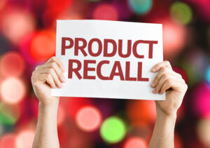 Hands holding product recall printed on a white paper with blurry lights in the background.