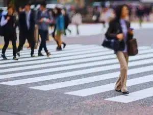 A group of people crossing a street at a crosswalk. Most individuals are walking in the same direction, and some are dressed in business attire.