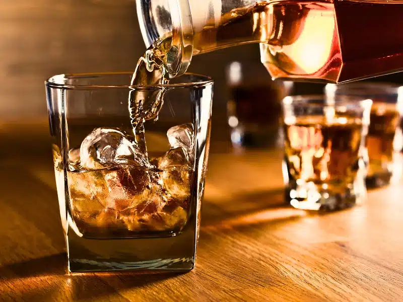 In Las Vegas bar a close up of a glass with liquor and ice in it, a bottle is filling the glass and there are a couple of glasses in the background. Liable for Overserving Alcohol