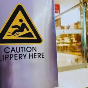A warning sign reading "Caution Slippery Here" inside a mall. average slip and fall settlement
