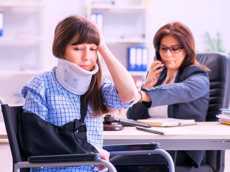 An injured woman in a neck brace sits near a lawyer. prove a slip and fall case
